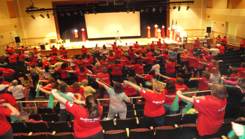 Follow the fifty women wearing red shirts doing stretching exercises with a band